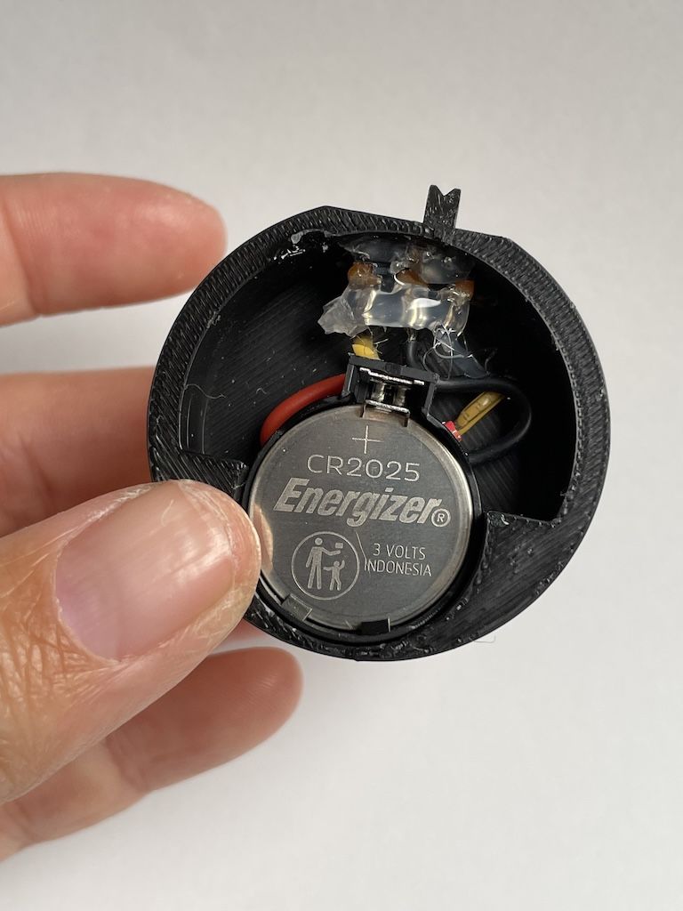 The bottom of the puck is shown. It's an open base with a small coin cell battery, showing soldered wires and hot glue.